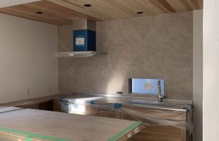 杉板の木天井と木目のキッチン収納が特徴のナチュラルモダンな新築キッチン。ニュアンスグレーの壁と大きなカウンターが設置された施工中の様子。