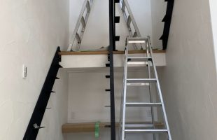 鉄骨フレームの階段を施工中の新築住宅。白い塗り壁の空間に黒い階段のラインが映える、吹き抜けと繋がるデザイン階段の工事風景。